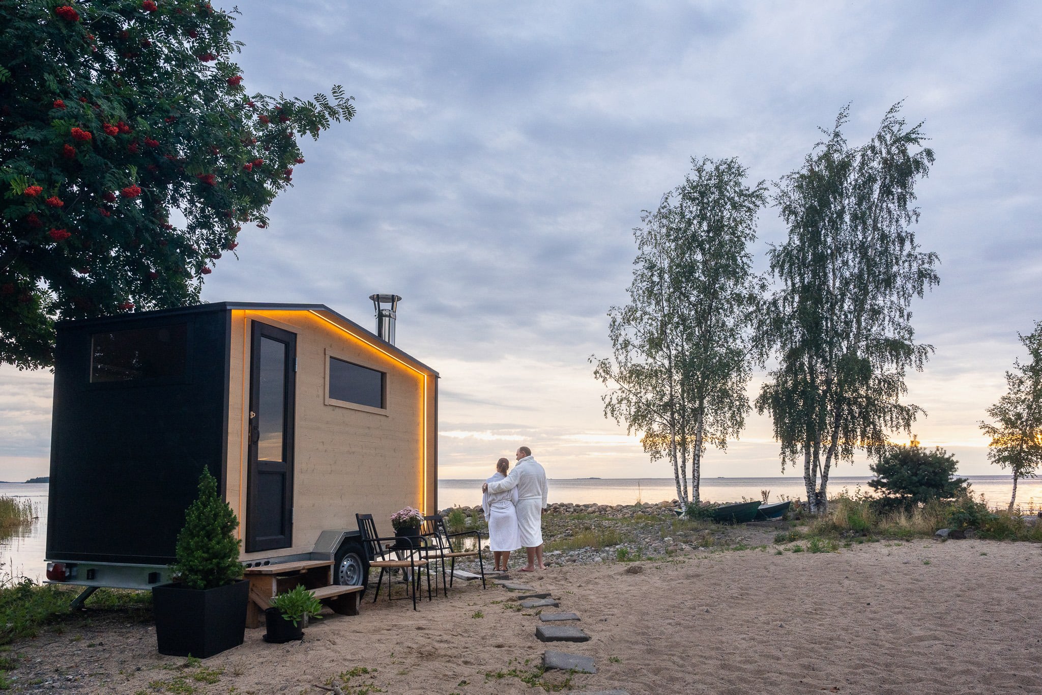 Proper Finnish Sauna carousel - small group sauna mood image AI lifestyle image of couple relaxing outside the mobile sauna in a scenic setting